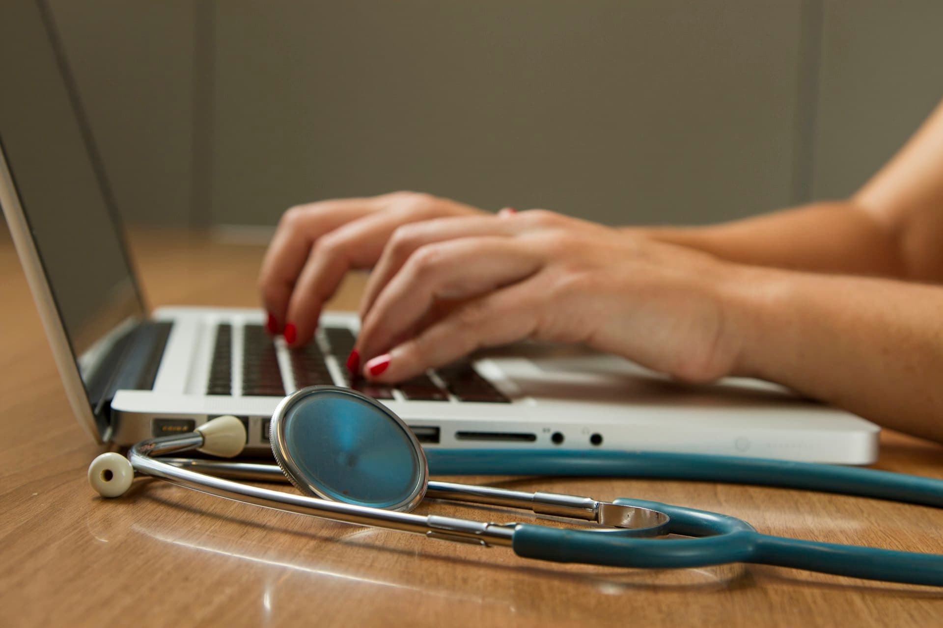 Doctor typing on a laptop beside a stethoscope